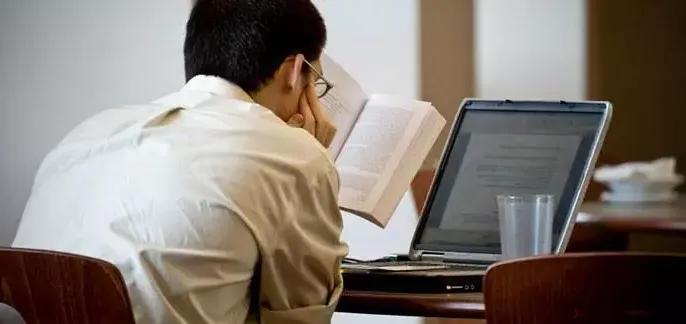 Distance Learning. Student reading a book and looking at a laptop